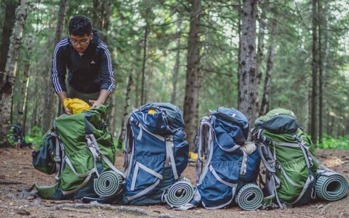 a line of backpacks rest on the ground while a student packs one of them